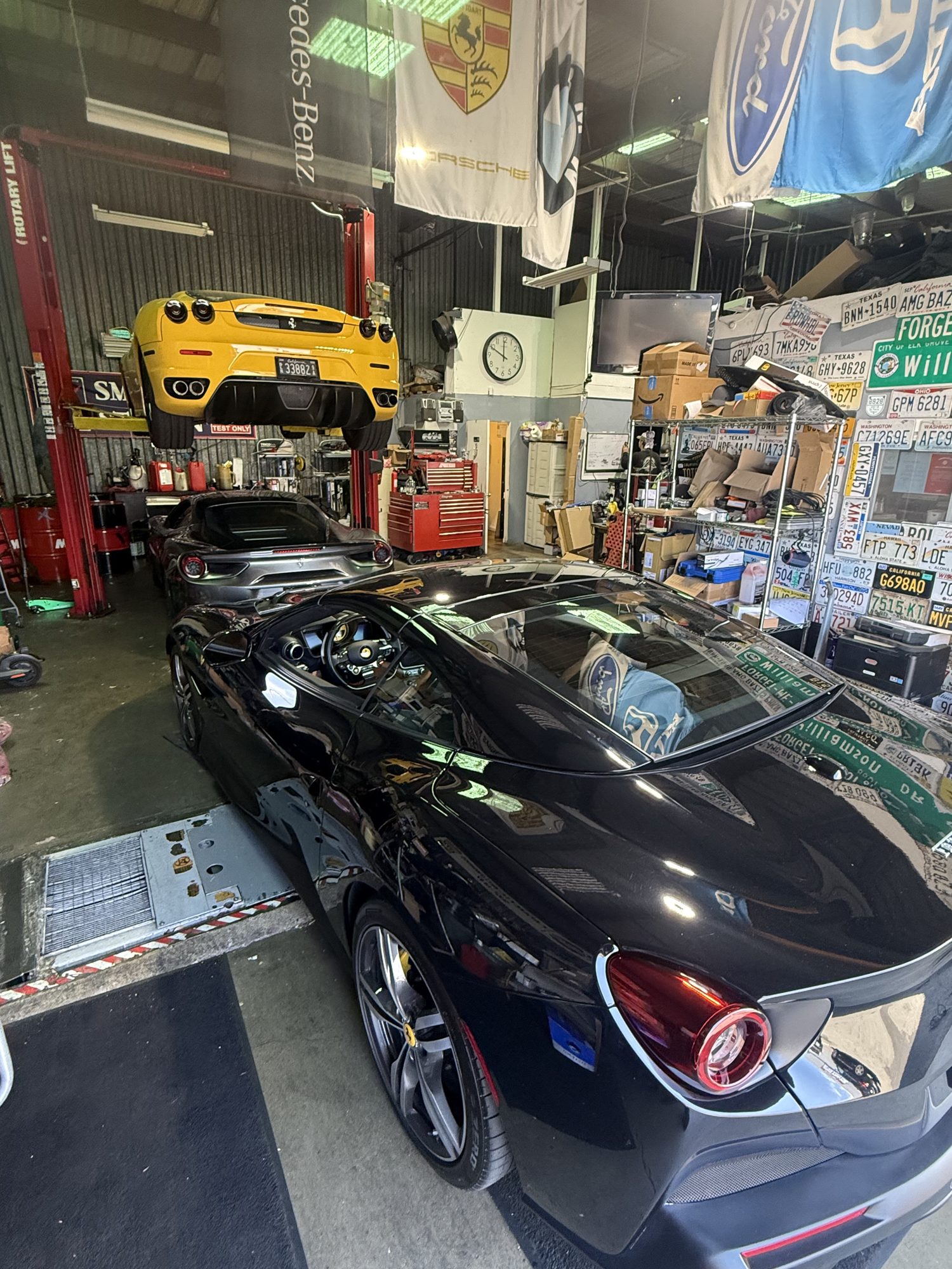 Inside the smogndash shop: a black Ferrari in the test bay, a yellow Ferrari on the lift, and walls lined with license plates